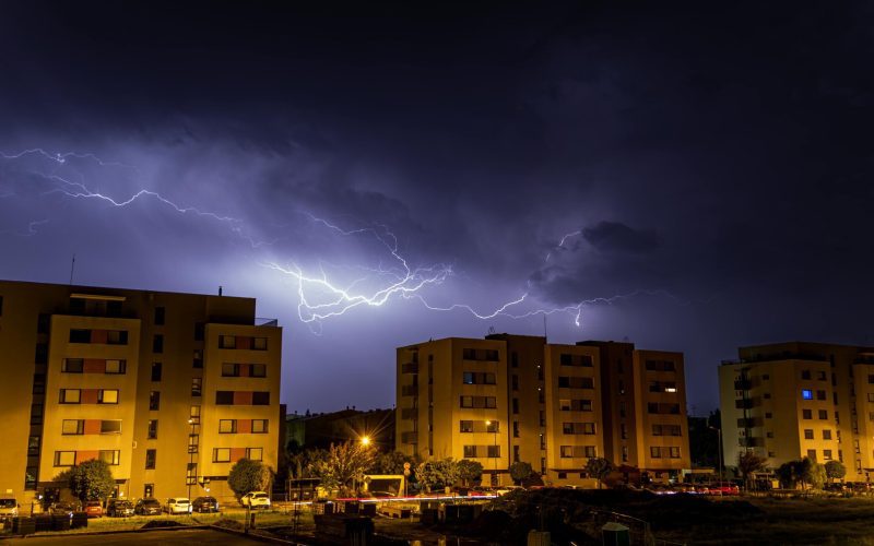 Lightning illuminates a dark sky over urban buildings at night.
